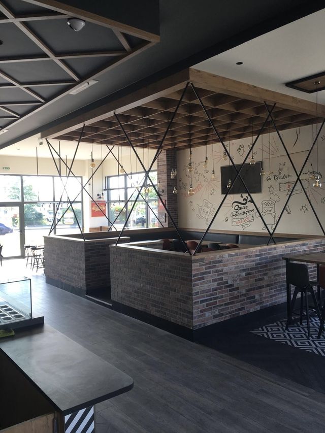 Salle de restaurant rénovée à Tours : séparations habillées de briques, plafond à caissons en bois, structures métalliques, suspensions et grandes baies vitrées