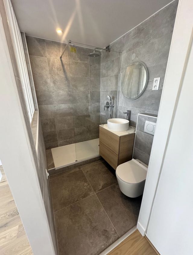 Salle d’eau avec douche, receveur extra-plat et paroi vitrée, carrelage gris grand format, meuble vasque bois et WC suspendu